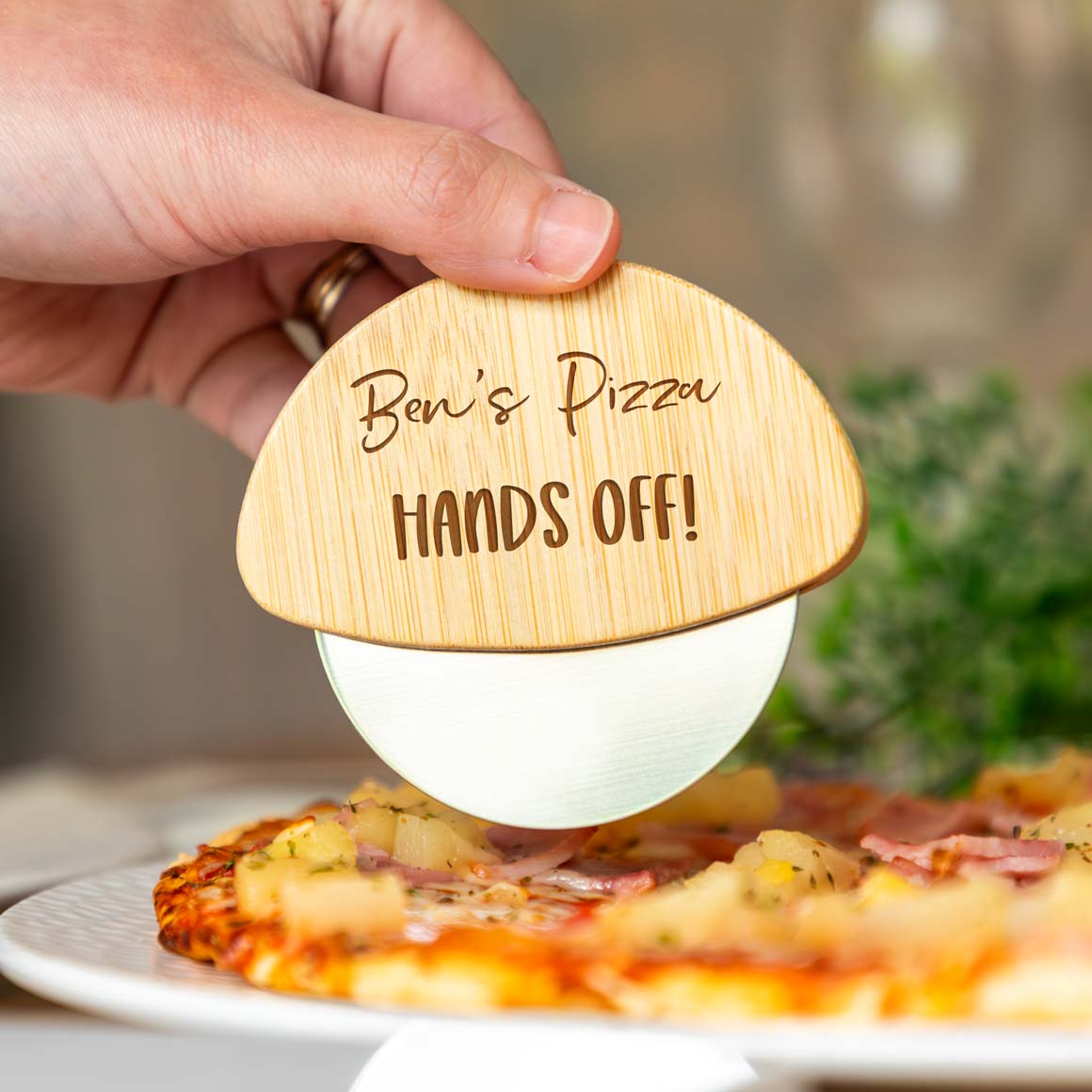Wooden pizza cutter engraved with 'Name's Pizza HANDS OFF!' above a pizza.