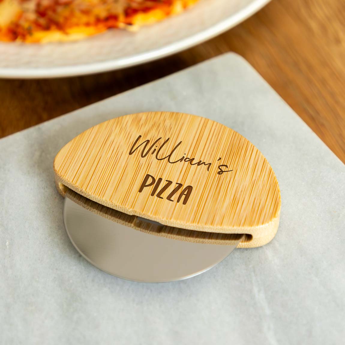 A wooden pizza cutter engraved with a name and 'Pizza' text, with a pizza in the background.