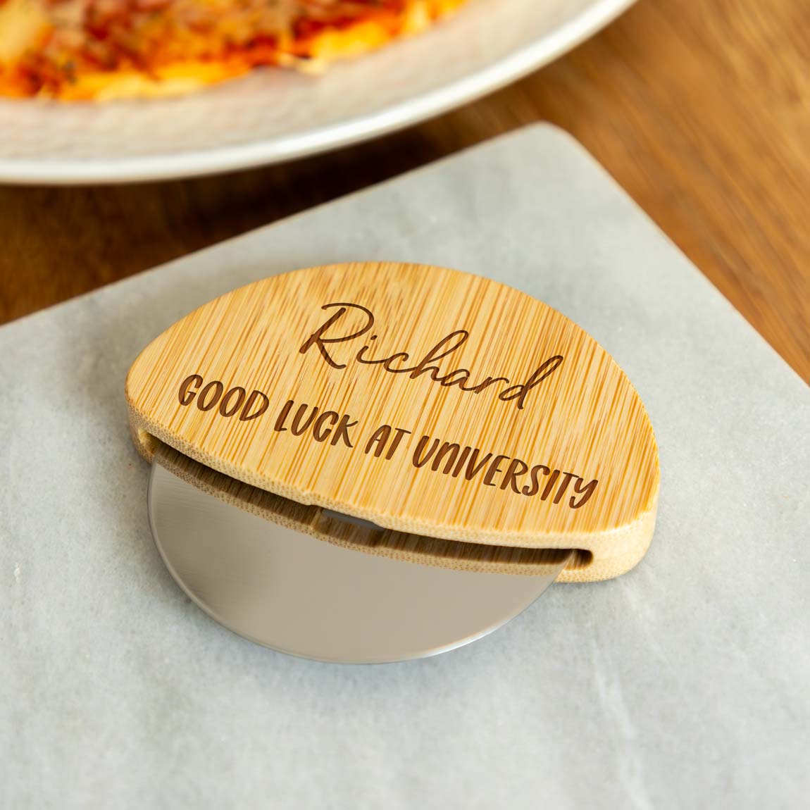 Wooden pizza cutter with engraved text on a table with a pizza in the background