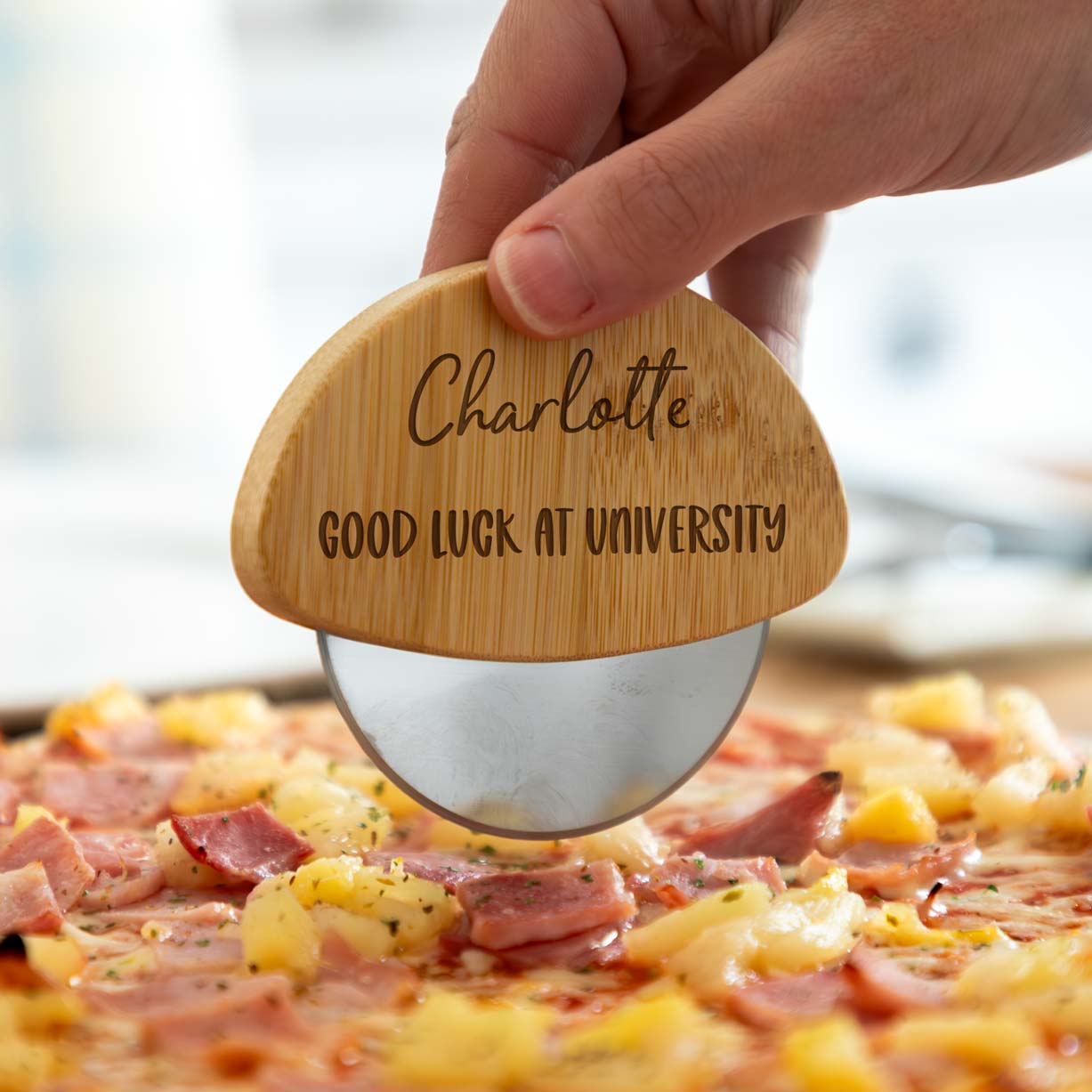 A person holding a wooden pizza cutter with an engraved name and 'good luck at university' text.