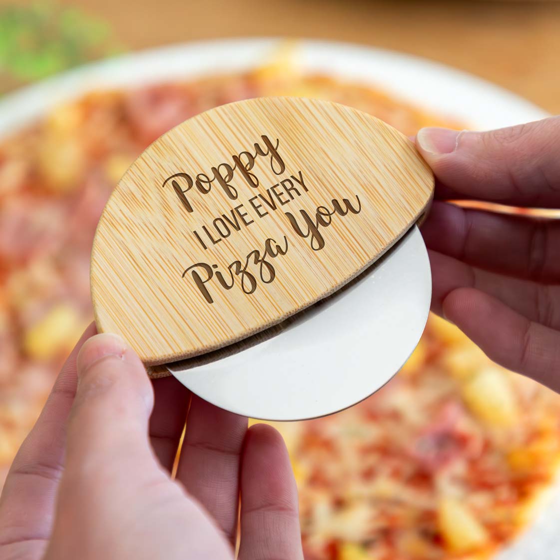 Wooden pizza cutter engraved with 'I Love Every Pizza You' text, held over a pizza.