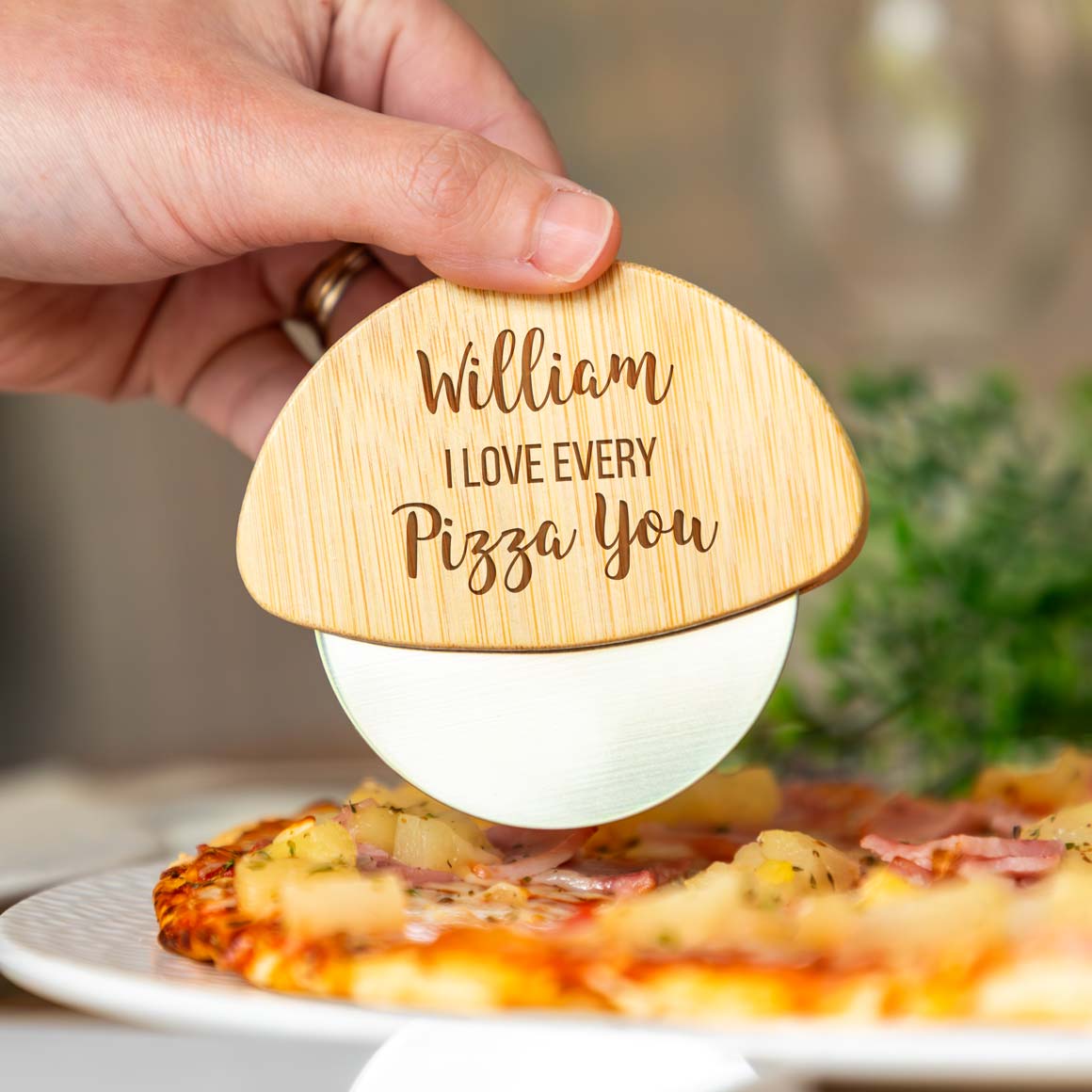 Wooden pizza cutter with engraved text held over a pizza