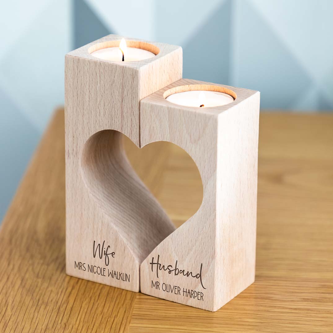 Wooden Wife and Husband candle holders forming a heart cut-out, personalised with full names, holding two lit tealights on a wooden table.