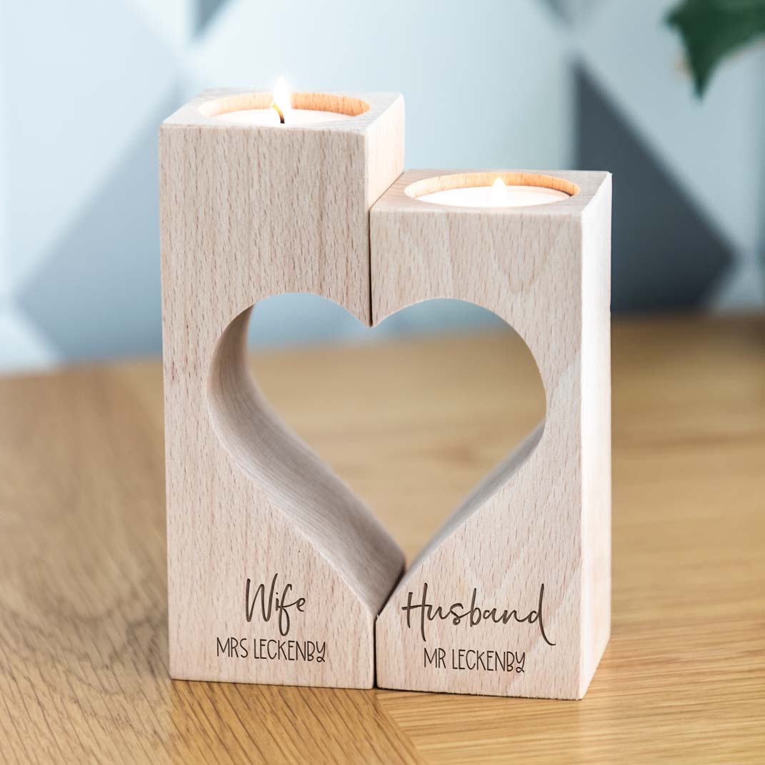 Front view of wooden Wife and Husband heart candle holders personalised with married names, holding two lit tealights on a wooden table.
