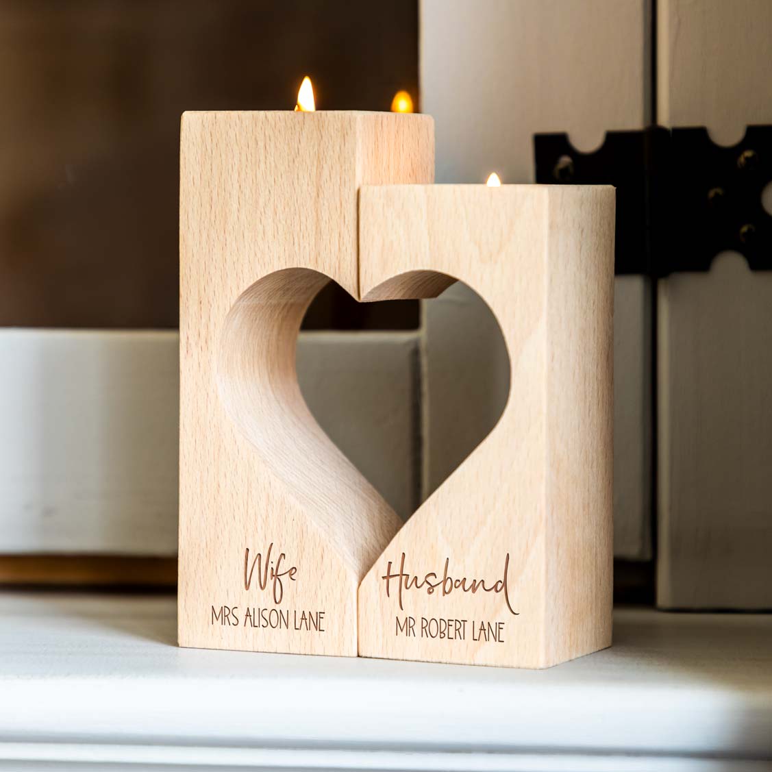 Personalised wooden Wife and Husband candle holder pair with a heart cut-out and two lit tealights, displayed on a white sideboard.