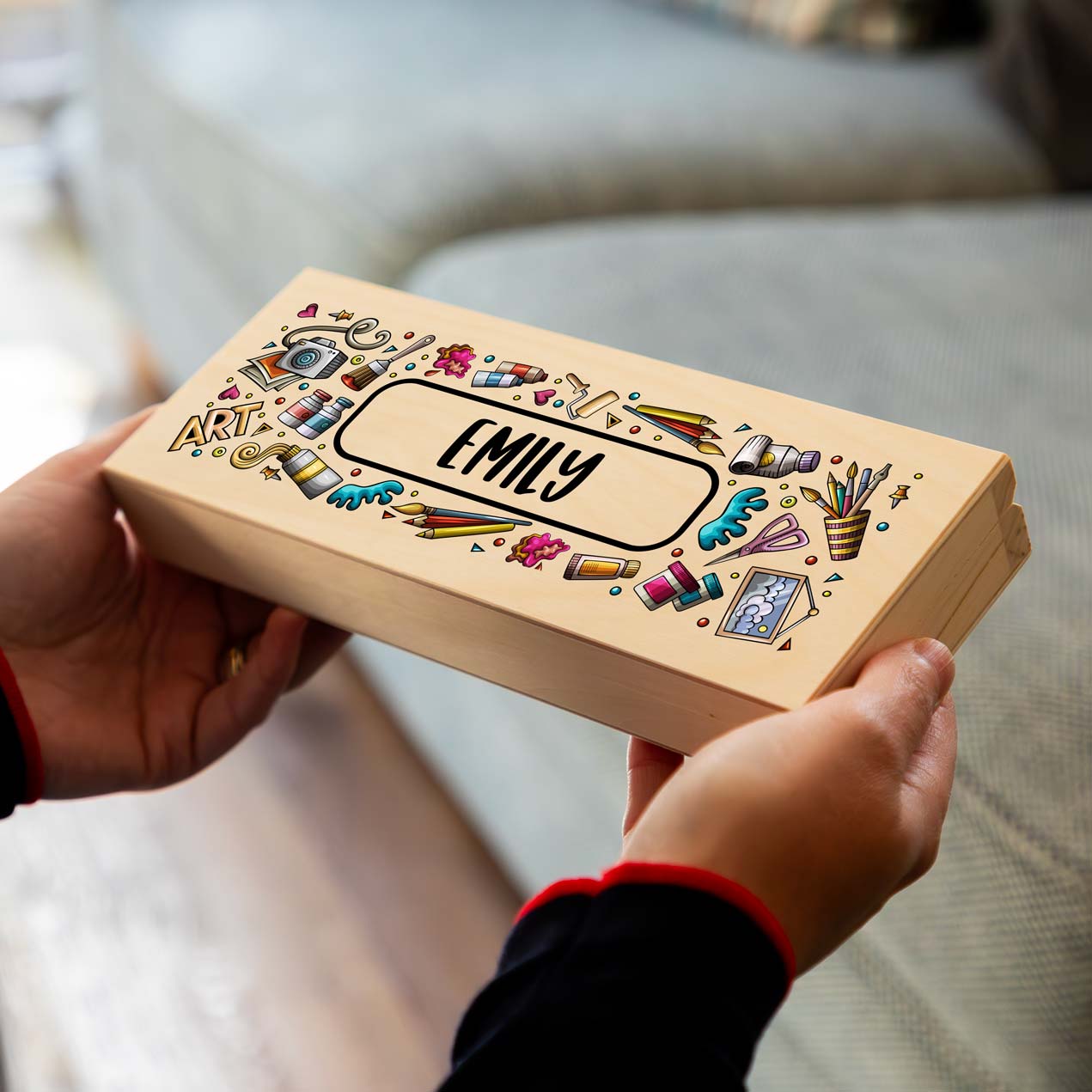 Wooden pencil case box printed with a personalised name and artistic illustrations held by a person.