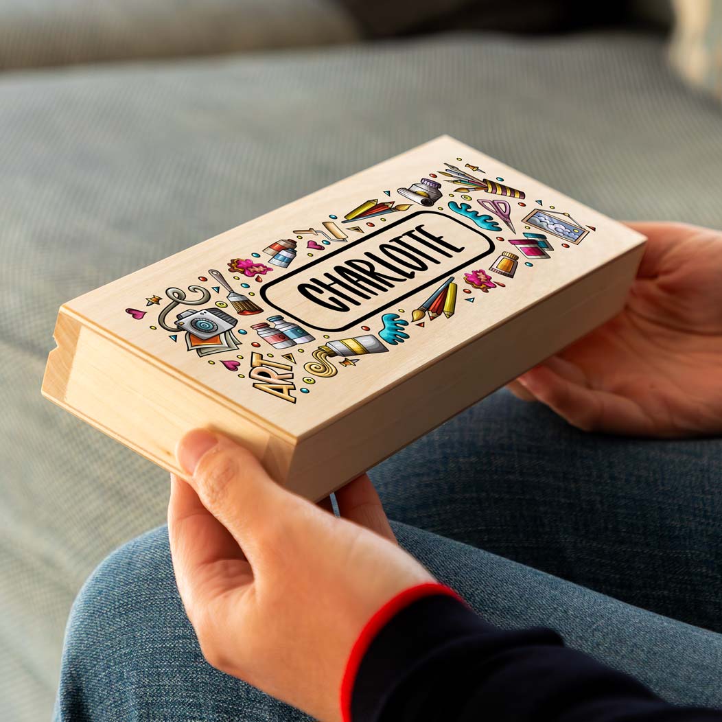 Person holding a wooden pencil case box printed with colourful illustrations and a personalised name.