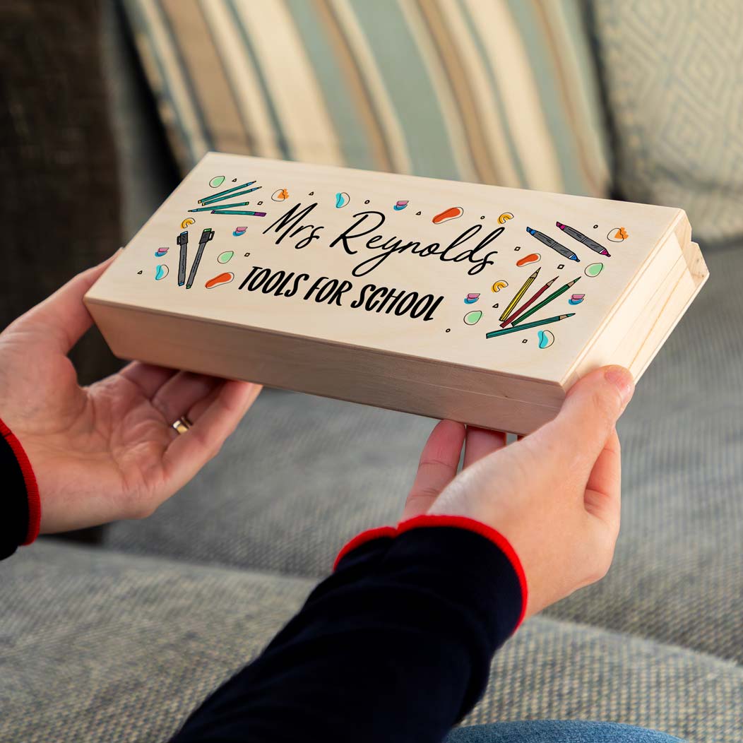Person holding a wooden pencil case that is personalised with a name and says 'Tools for School' with colourful illustrations.