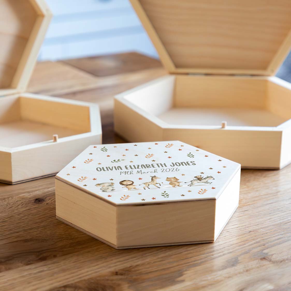 Wooden hexagonal new baby keepsake box with personalised text and jungle animal illustrations on a wooden surface.
