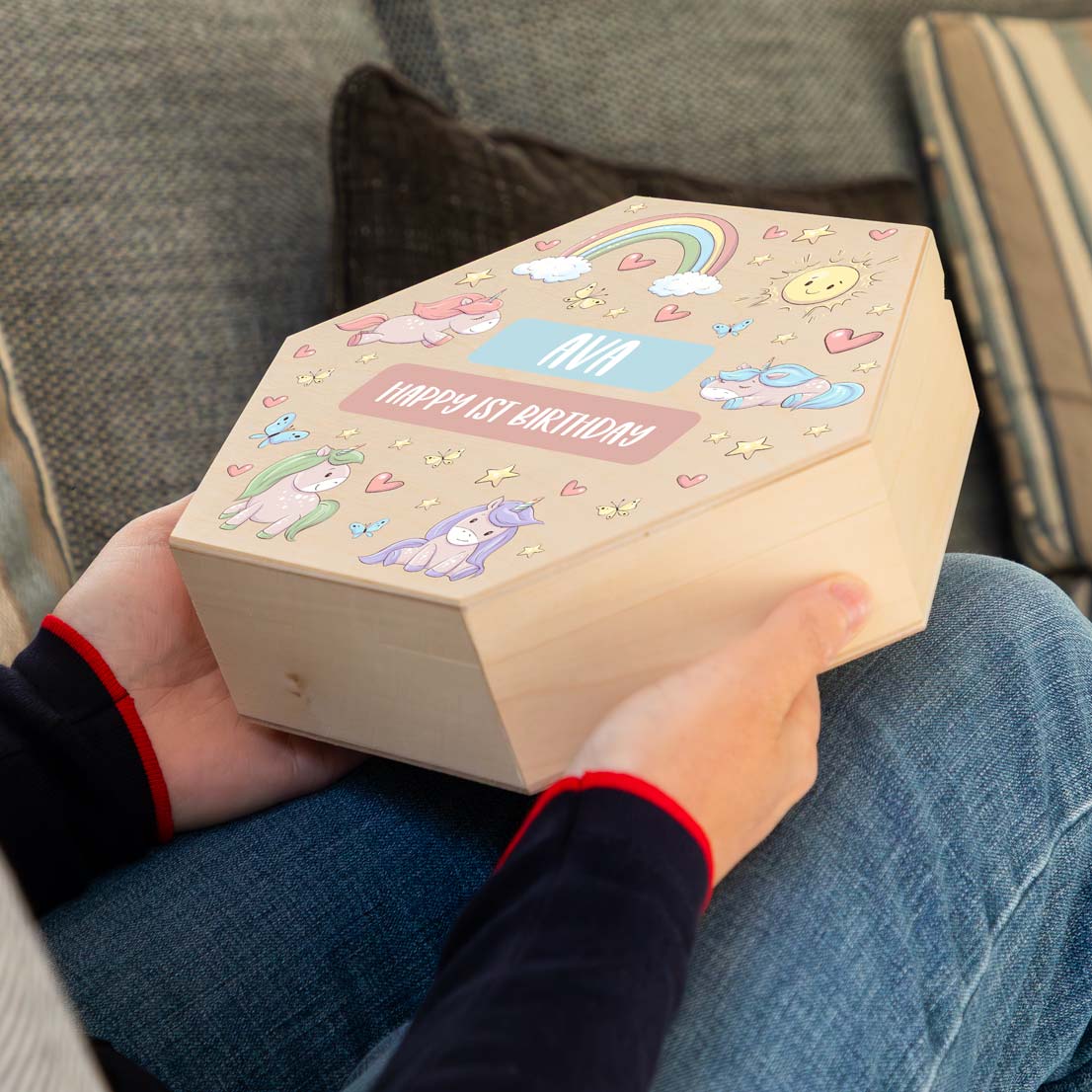 Person holding a wooden keepsake box with colourful unicorn designs and personalised text, to celebrate a 1st birthday.