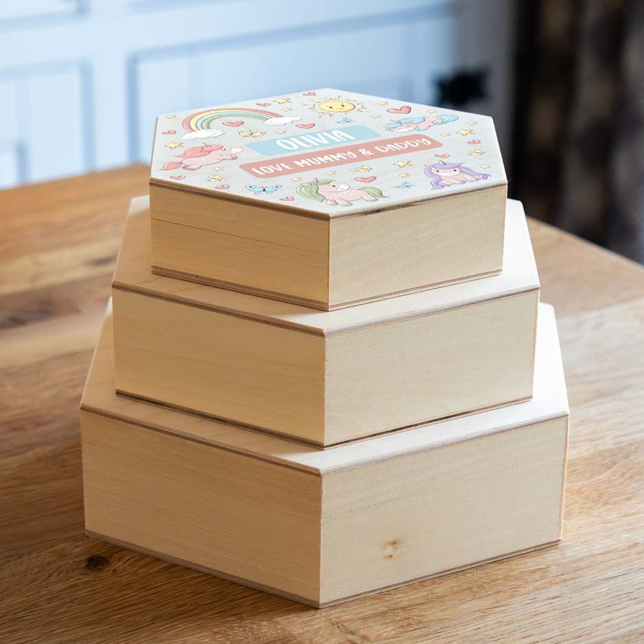 Stack of wooden hexagonal keepsake boxes with decorative lids on a wooden surface.