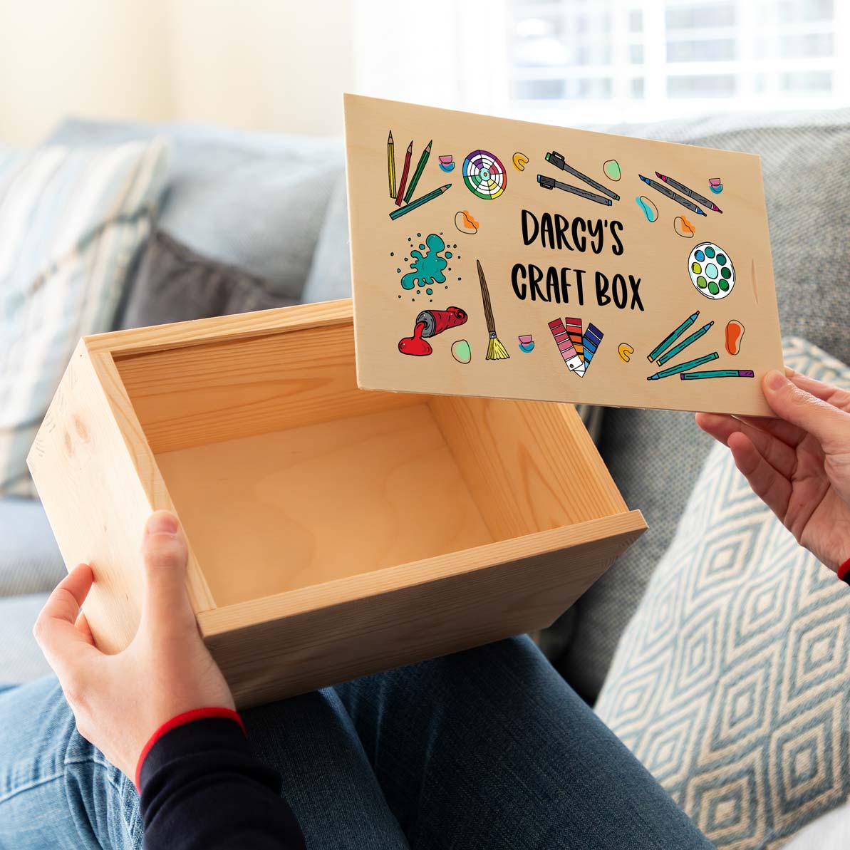 Wooden craft box with a personalised design on the sliding lid held by a person on a couch.