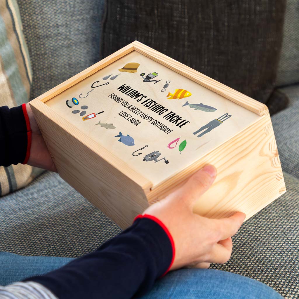 Wooden fishing tackle box with fishing-themed illustrations and personalised text, held by a person on a couch.