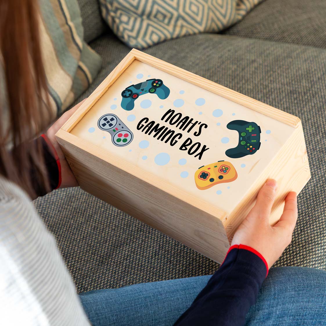 Wooden gaming box printed with personalised text and gaming controller designs, held by a person on a couch.