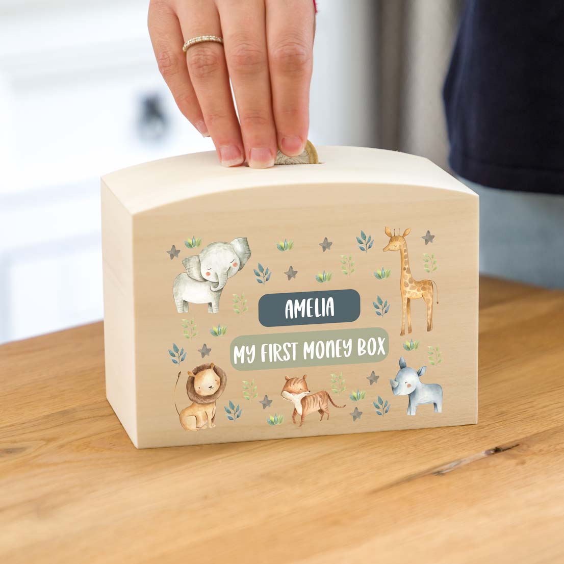 Children's money box with animal illustrations, personalised with a name and  'My First Money Box' text on a wooden surface.