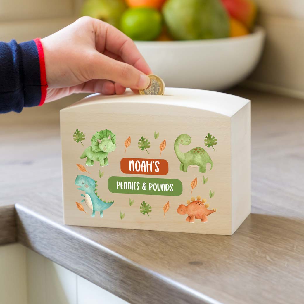 Wooden money box printed with a dinosaur design and personalised text on a wooden surface.