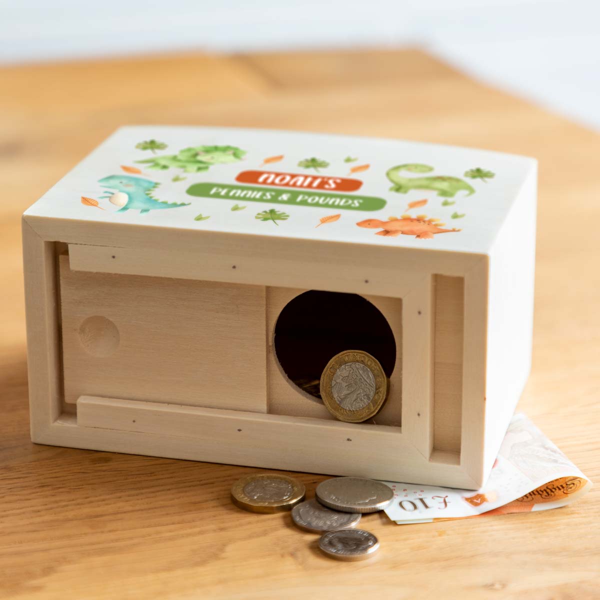 Wooden money box with dinosaur design with a sliding opening on the bottom to access the money inside.