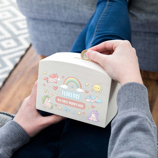 Person depositing a coin into a personalised money box printed with a unicorn design.