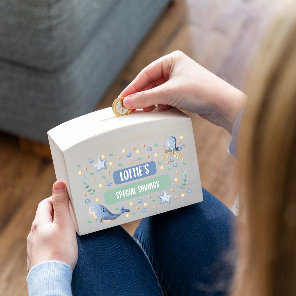 Person depositing a coin into a personalised children's money box with a sea animals design.