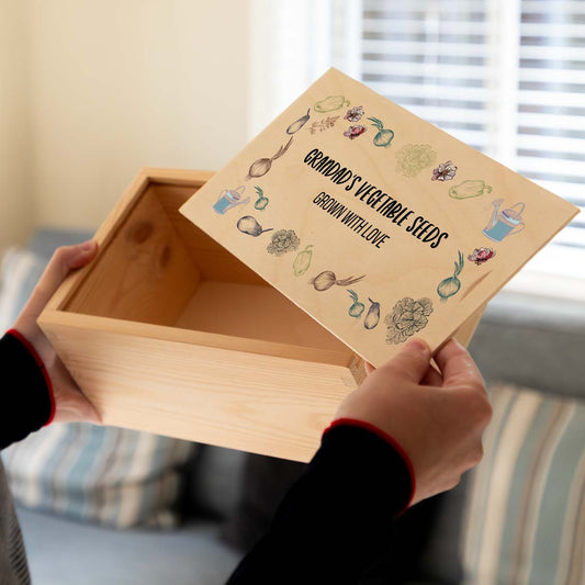Person holding a wooden vegetable seed box with personalised text and vegetable illustrations.