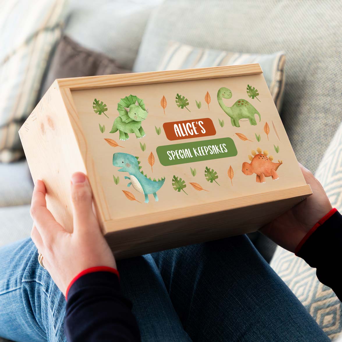 Wooden keepsake box with dinosaur illustrations and the personalised name followed by 'Special Keepsakes' text, held by a person.