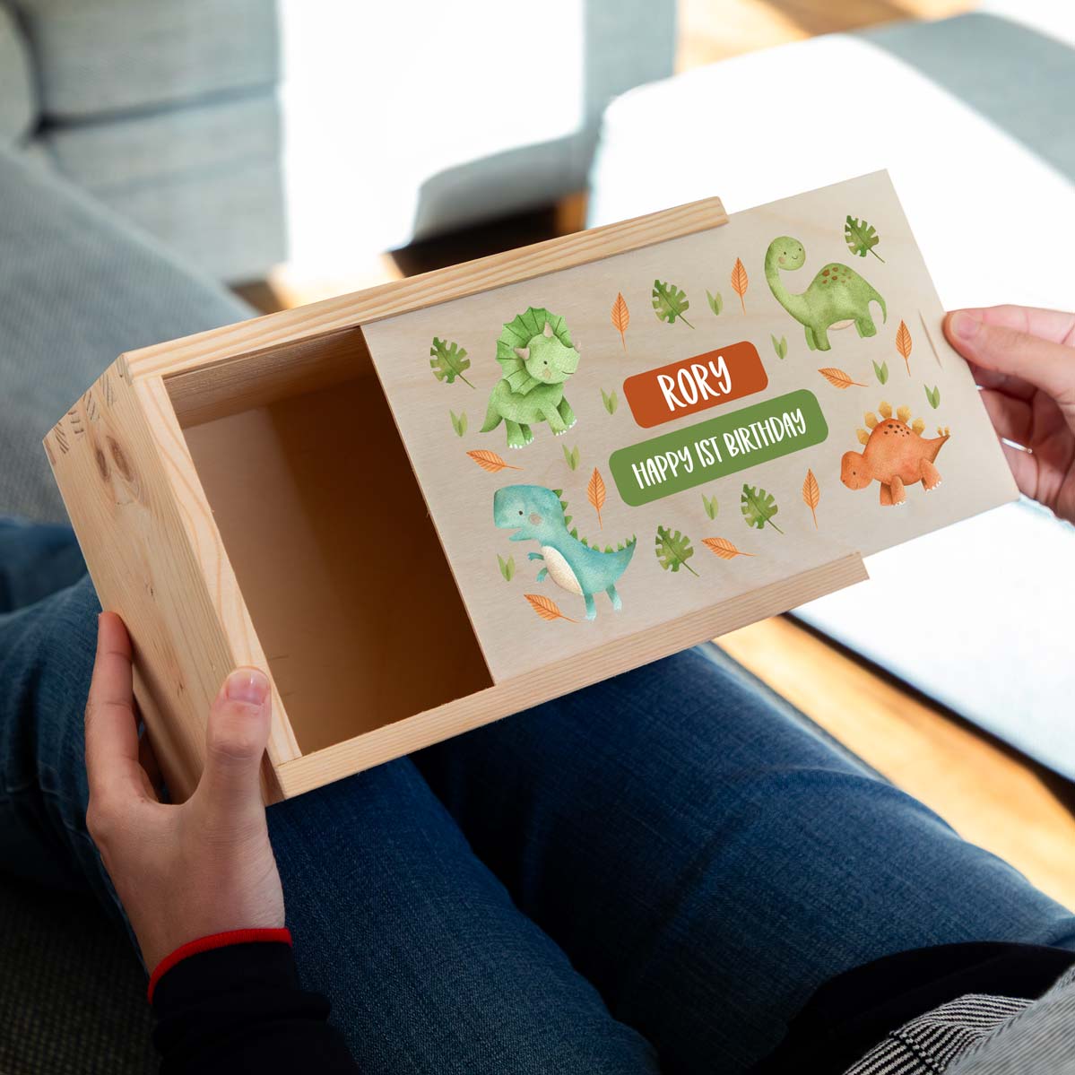 Wooden keepsake box with dinosaur illustrations and personalised text held by a person