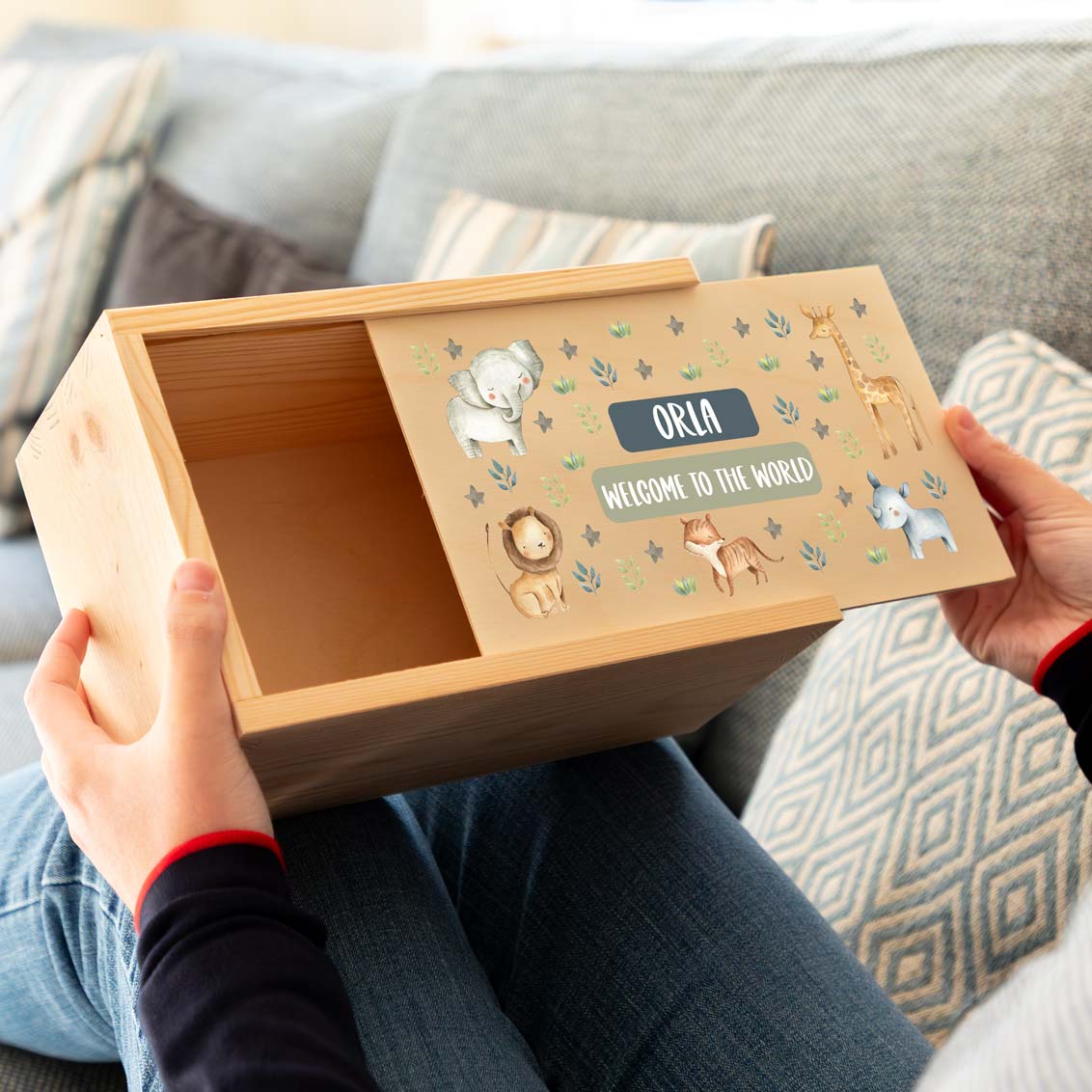 Wooden keepsake box new baby gift with animal illustrations and personalised text held by a person on a couch.