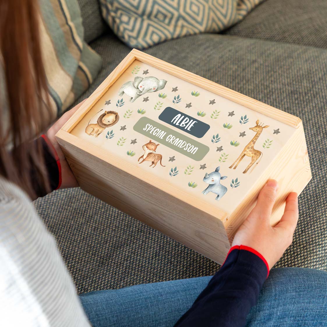 Person holding a wooden keepsake box with jungle animal illustrations and personalised text to celebrate a new grandchild.