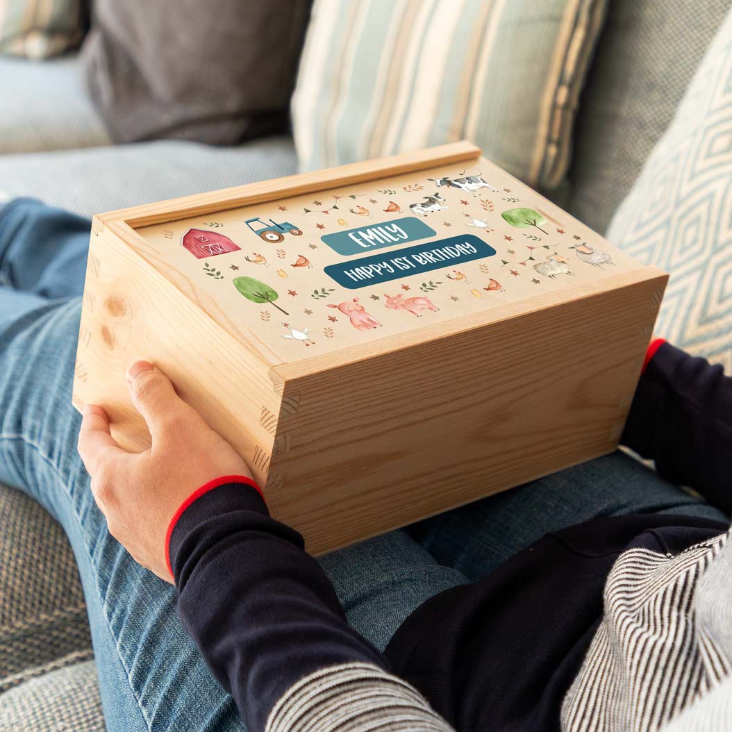Person holding a wooden keepsake box with farm animal illustrations and personalised  text to celebrate a 1st birthday.