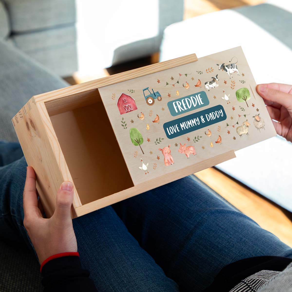Wooden keepsake box with personalised farm animals design held by a person, sitting on a couch.
