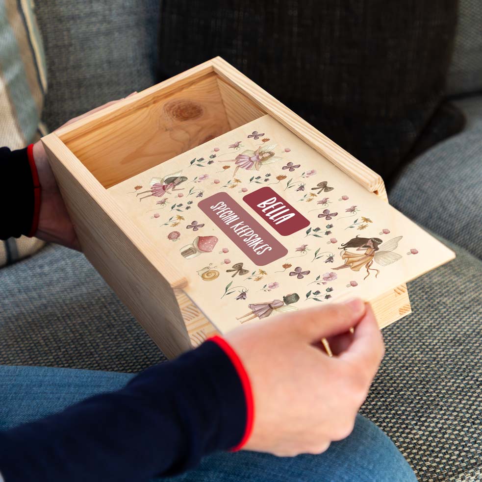 Wooden keepsake box with decorative lid featuring fairy illustrations and text, held by a person.