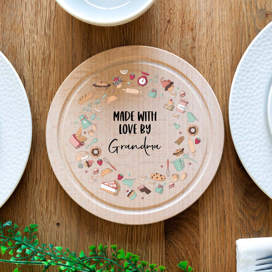 Wooden cake board with baking illustrations and says 'Made with love by' followed by the personalised name.