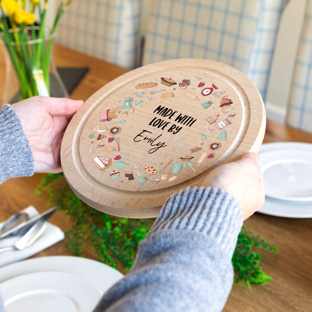 Person holding a wooden cake board with decorative patterns and personalised text on a table setting.