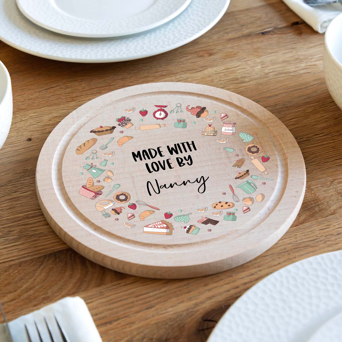 Round wooden cake serving board with colourful baking illustrations and personalised  text on a wooden table.