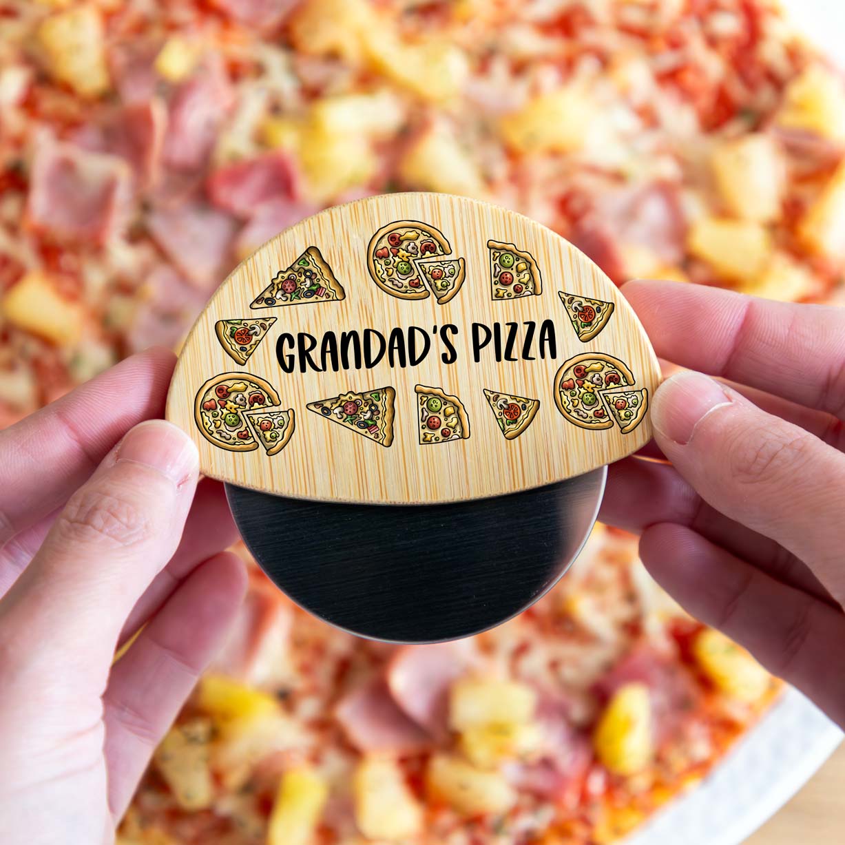 Wooden pizza cutter wheel with personalised text held over a pizza.