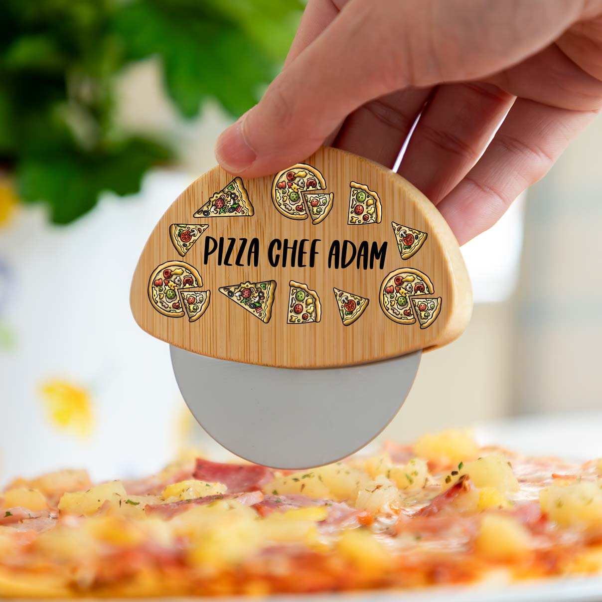 Personalised pizza cutter wheel with printed text and pizza designs, held over a pizza.