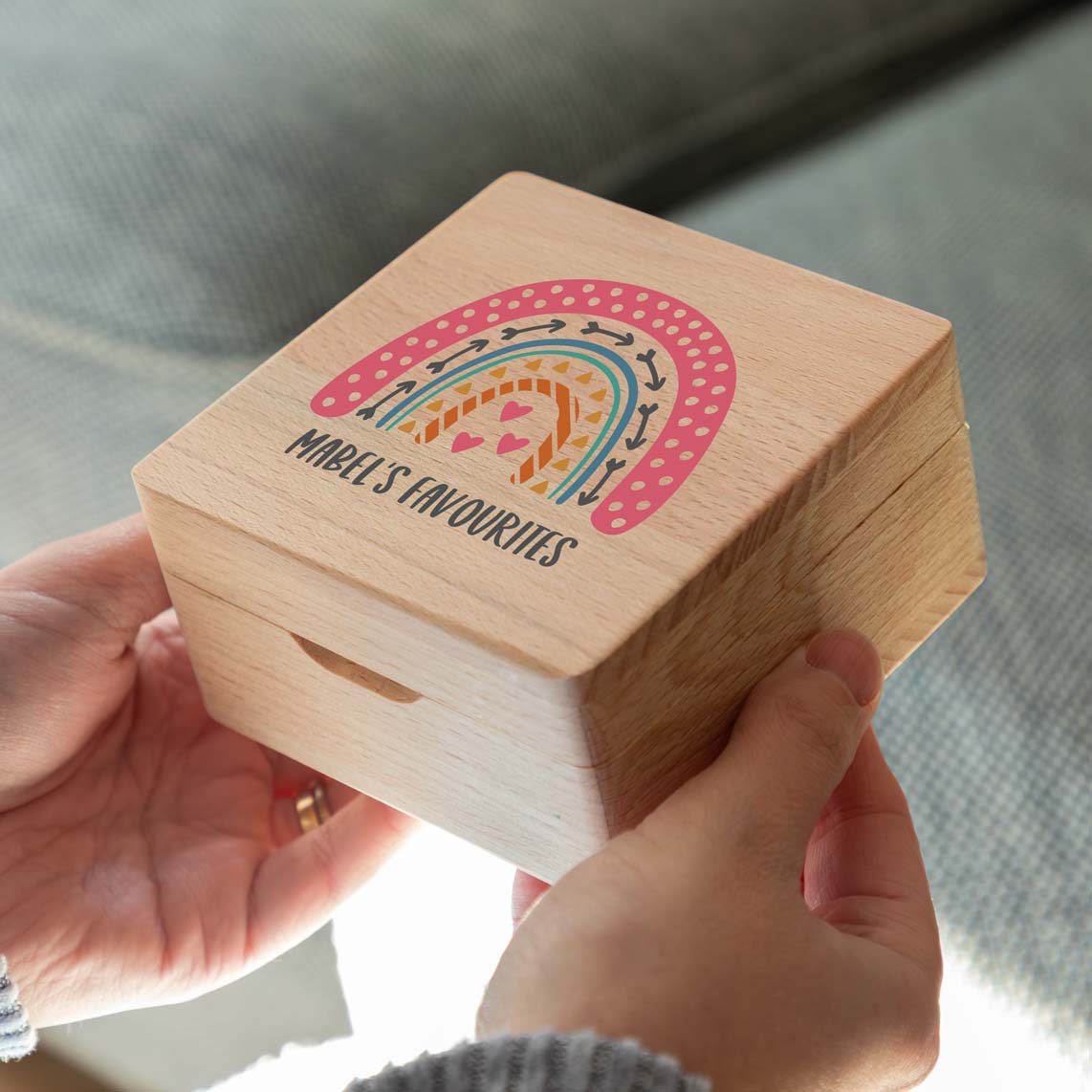 Wooden jewellery box held in two hands, with a colourful rainbow and personalised text printed on the lid.