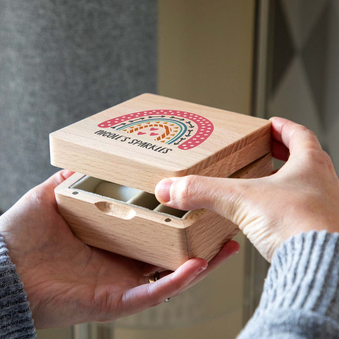 Hands opening a wooden jewellery box with a colourful rainbow and personalised text printed on the lid.