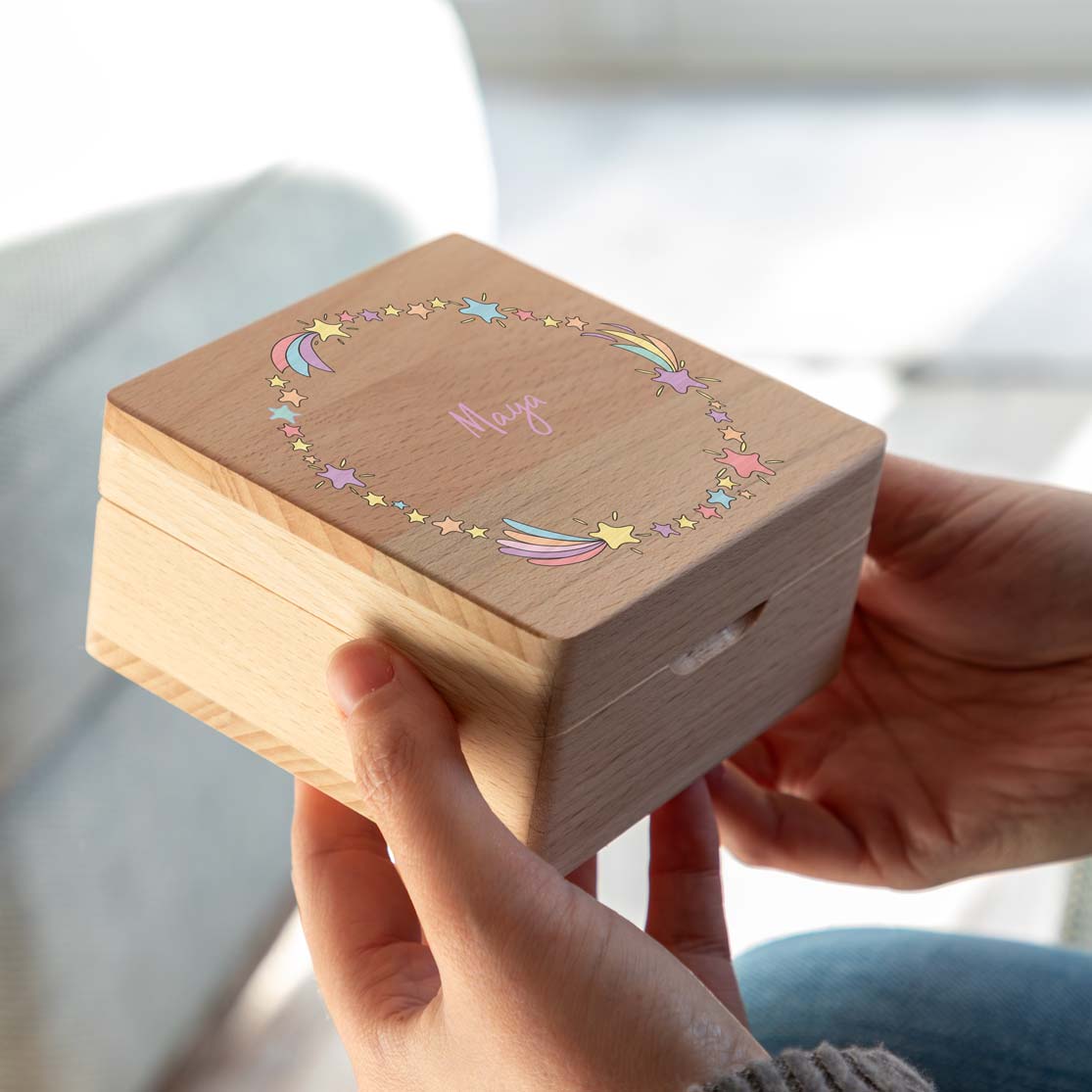 Square wooden jewellery box with colourful shooting stars surrounding a personalised name, held in two hands.