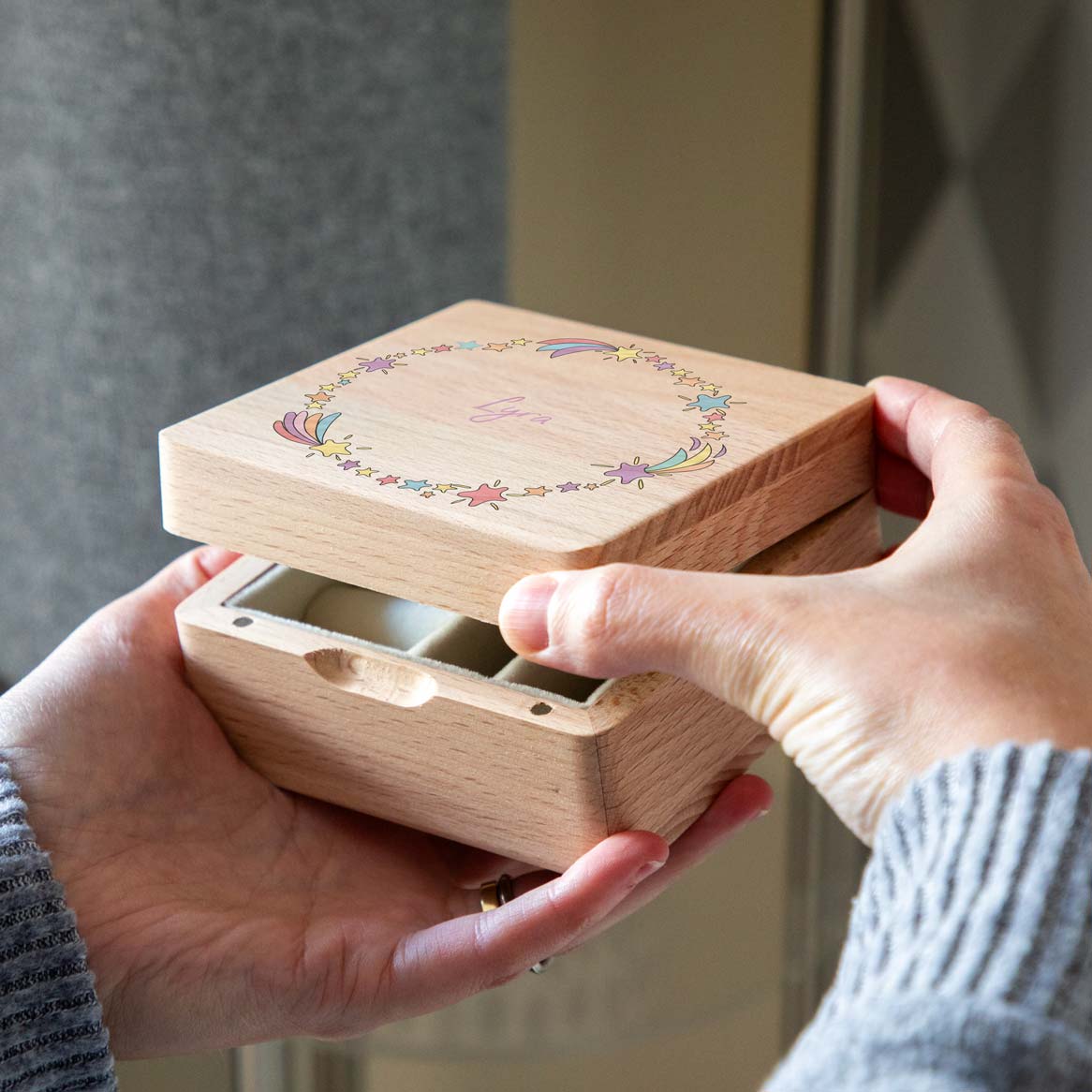 Personalised wooden jewellery box with colourful shooting stars, held in two hands with the lid partially open.
