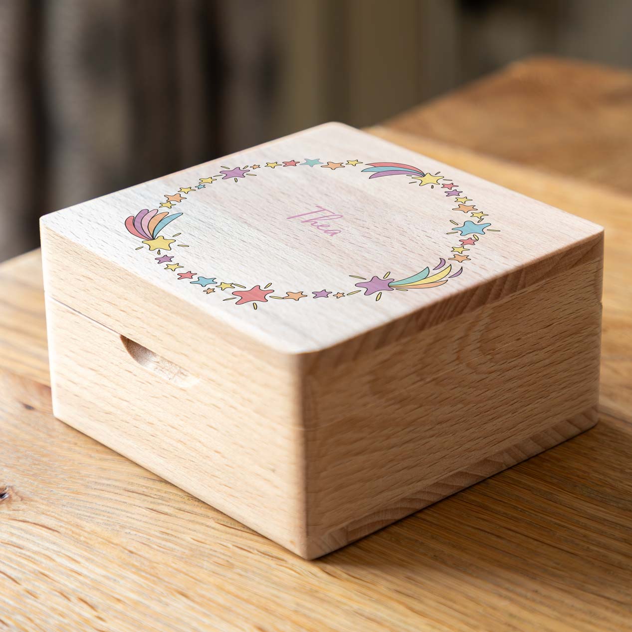 Closed wooden jewellery box on a wooden table, with colourful shooting stars surrounding the personalised name on the lid.
