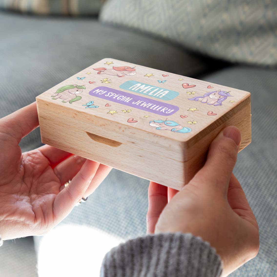 Wooden jewellery box with colourful unicorns and the personalised text, held in two hands.