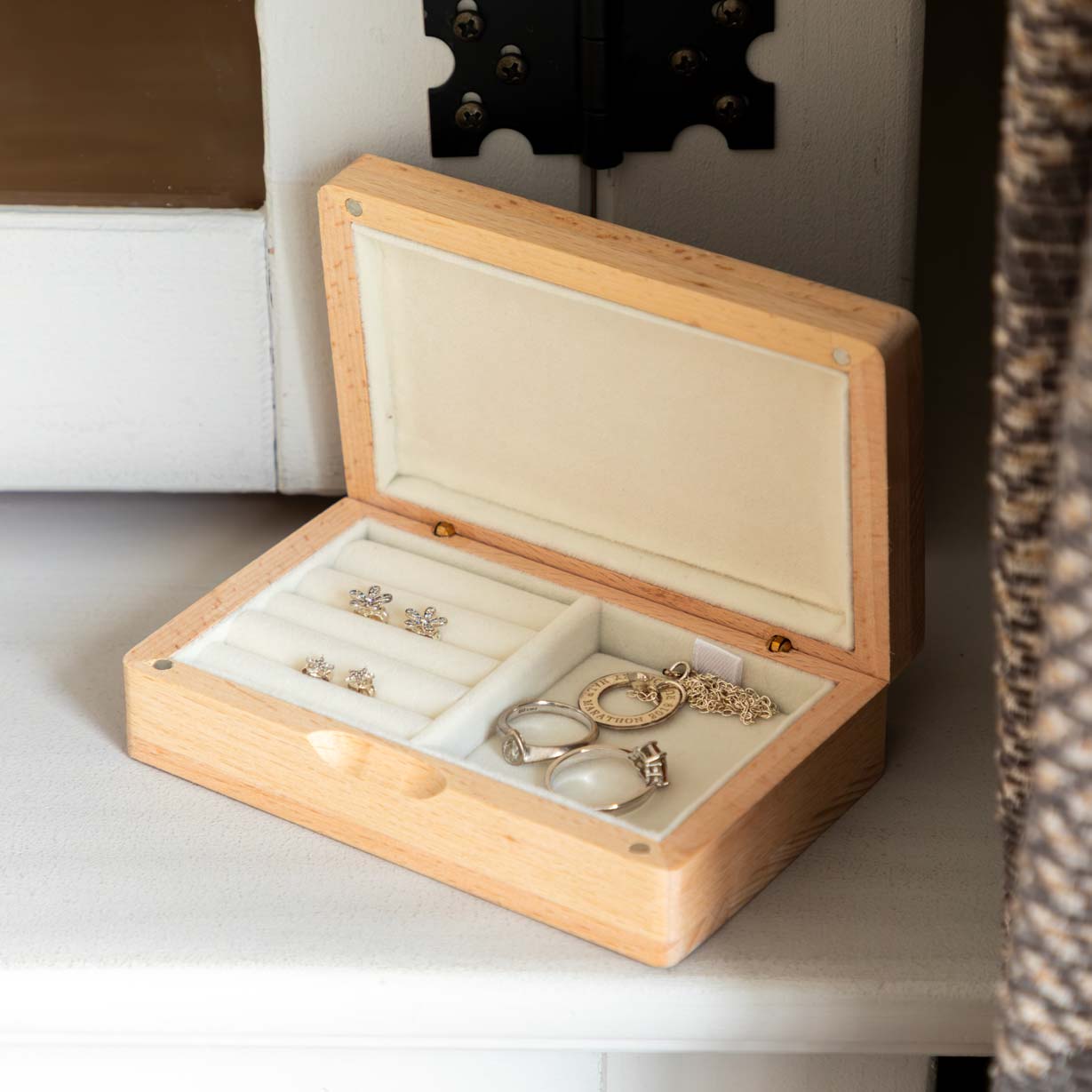 Open wooden jewellery box with cream-lined ring rolls and compartments holding earrings, rings and a necklace.