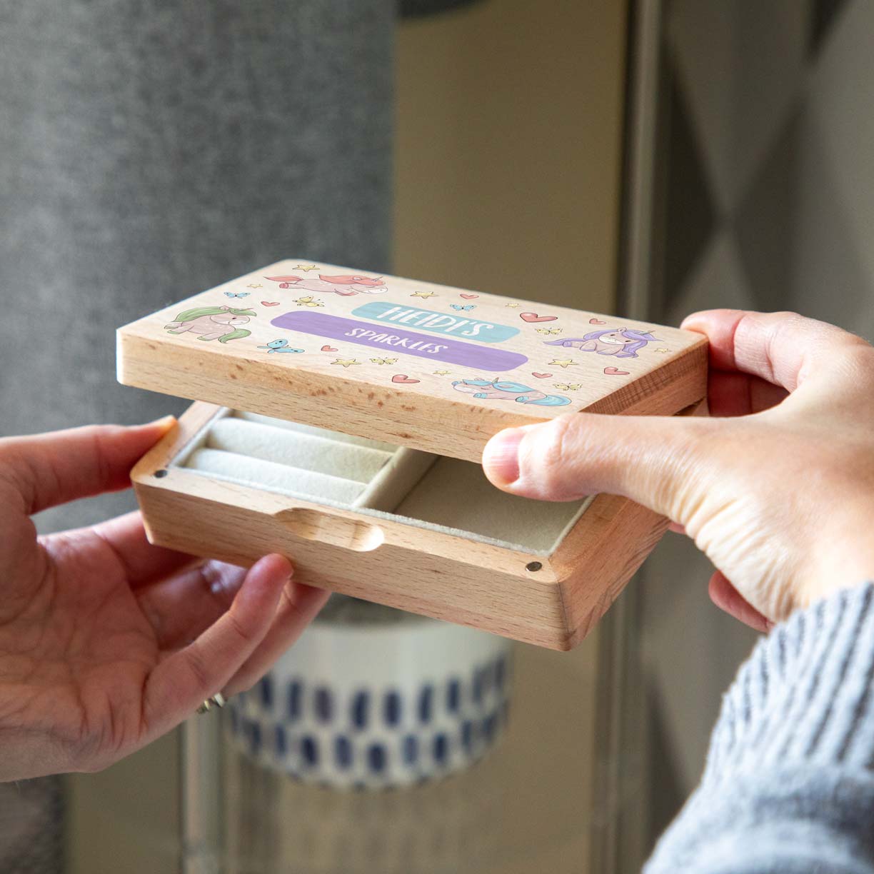 Hands opening a wooden unicorn jewellery box personalised with custom text, revealing cream-lined compartments.