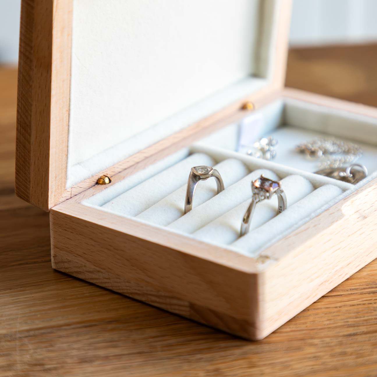 Close-up of two rings nestled in cream-lined ring rolls inside an open wooden jewellery box.