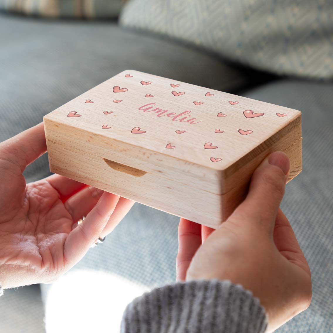 Wooden jewellery box with pink hearts and the personalised name on the lid, held in two hands.