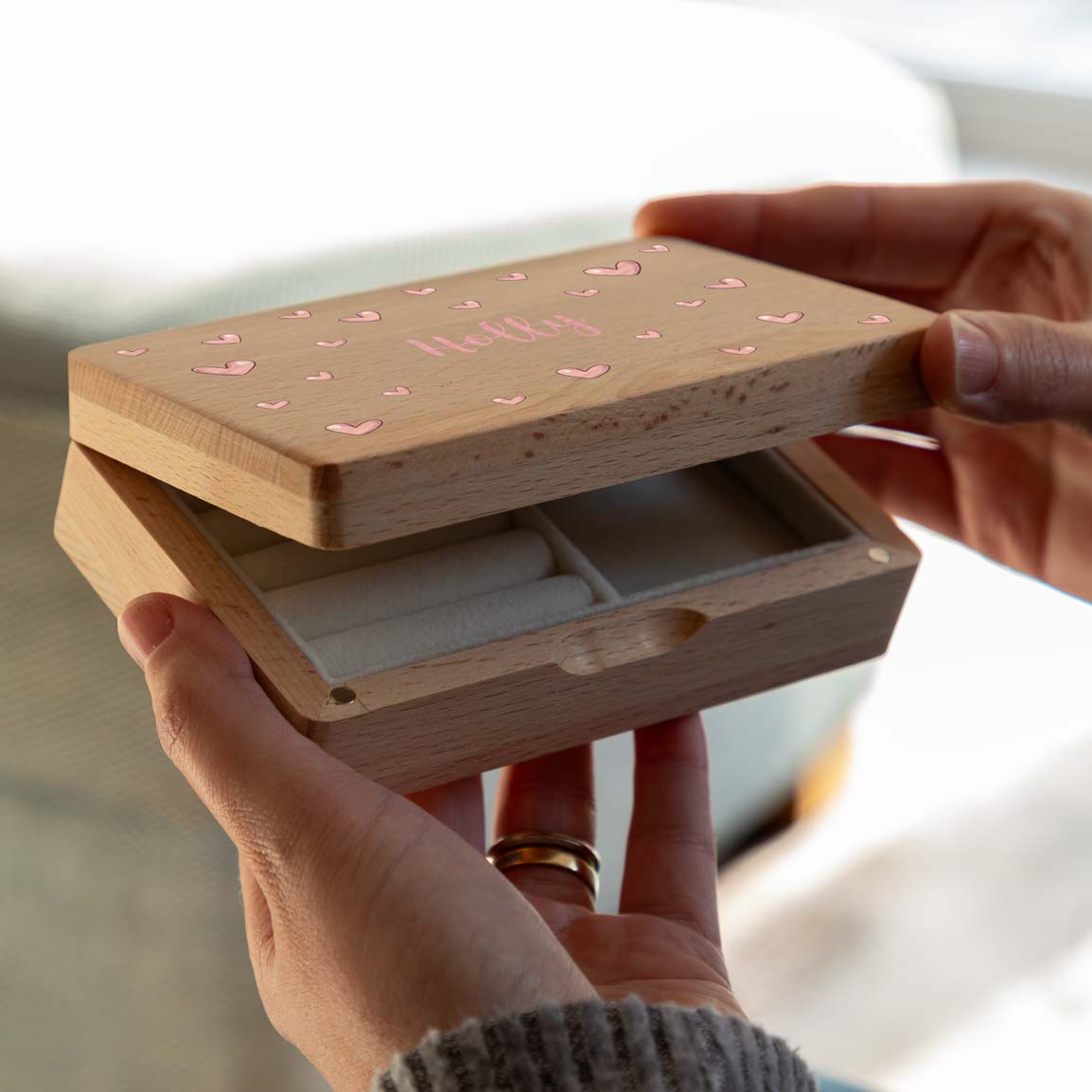 Hands opening a personalised Little Hearts jewellery box to reveal its cream-lined compartments.