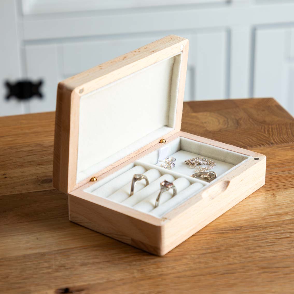 Open wooden jewellery box on a table, with rings in padded rolls and jewellery in the side compartment.
