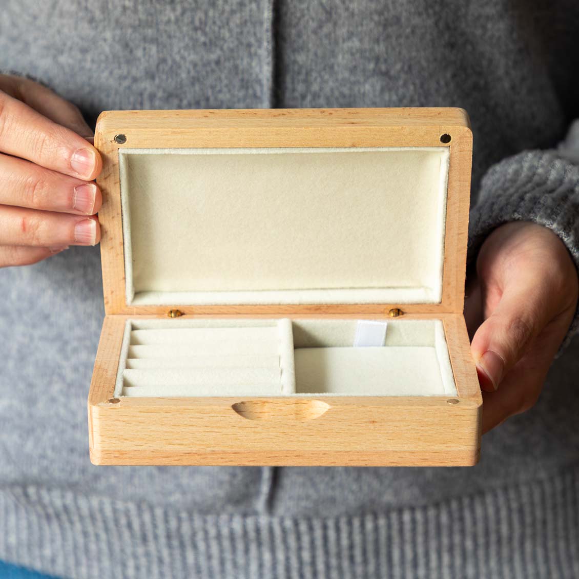 Open rectangular wooden jewellery box held up to show empty cream-lined ring rolls and storage compartments.